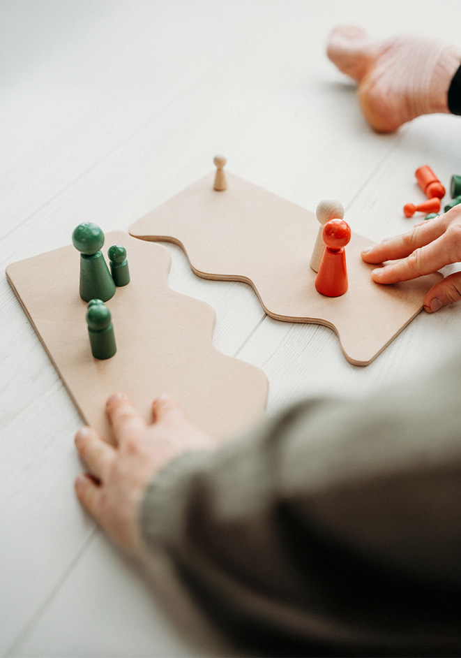Hände ordnen bunte Holzfiguren auf Holzplatten (systemische Aufstellung).